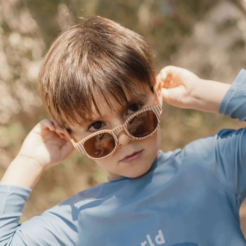 Occhiali da sole Little Dutch con montatura marrone e strisce blu, indossati in un contesto di vita quotidiana.